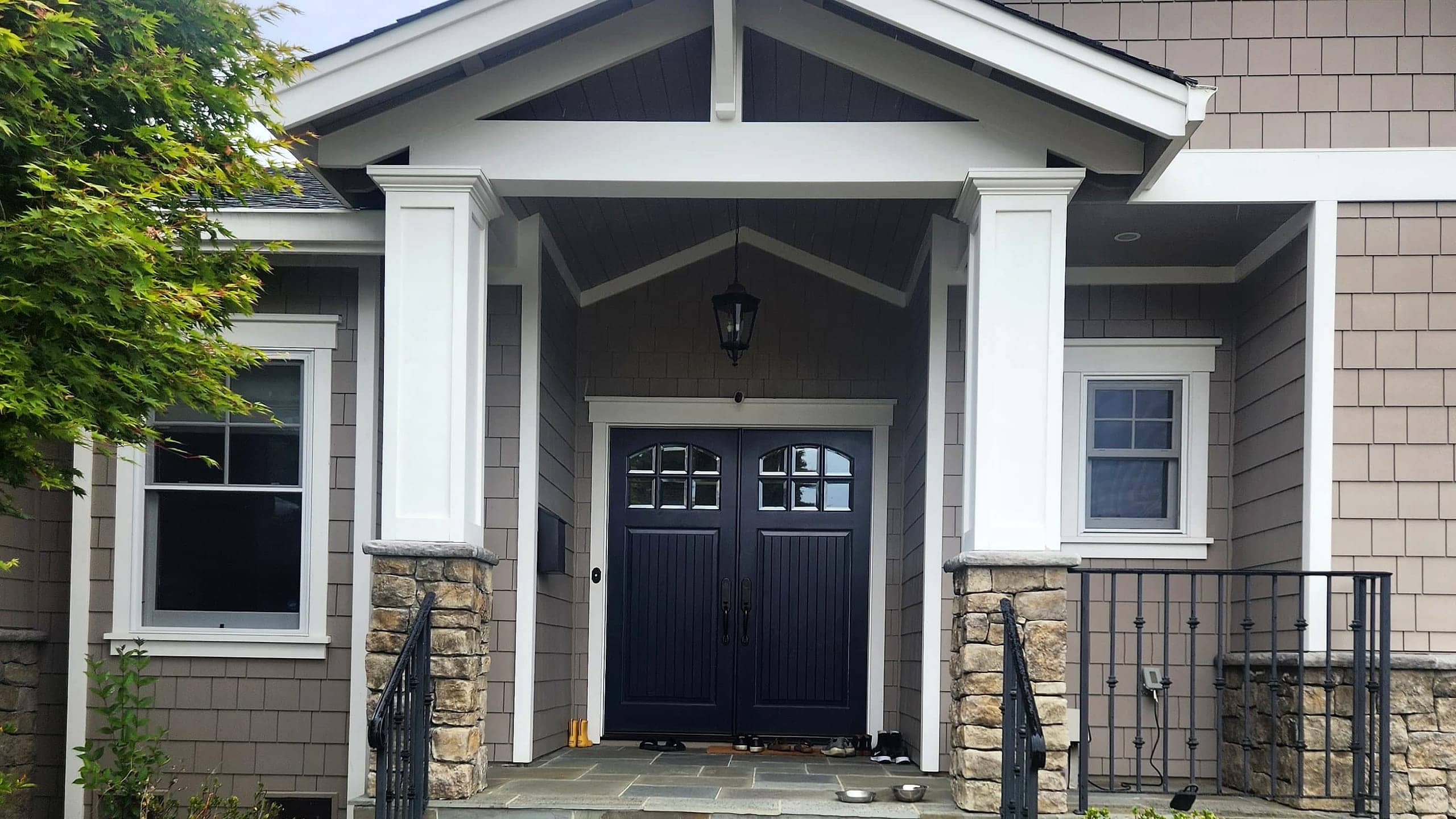 Freshly repainted Craftsman entry with taupe shingle siding, white columns, and a black double front door